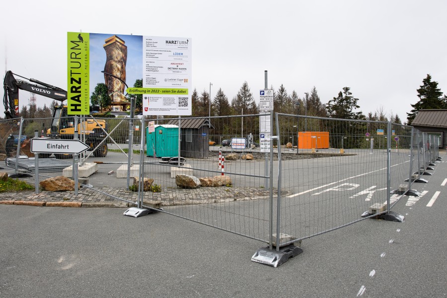 Ein Bauschild für den «Harzturm» ist auf einem Großraumparkplatz neben einem Bagger eingezäunt. Geplant ist ein hier 65 Meter hoher Aussichtsturm mit einer gläsernen Plattform und einer Rutsche. 