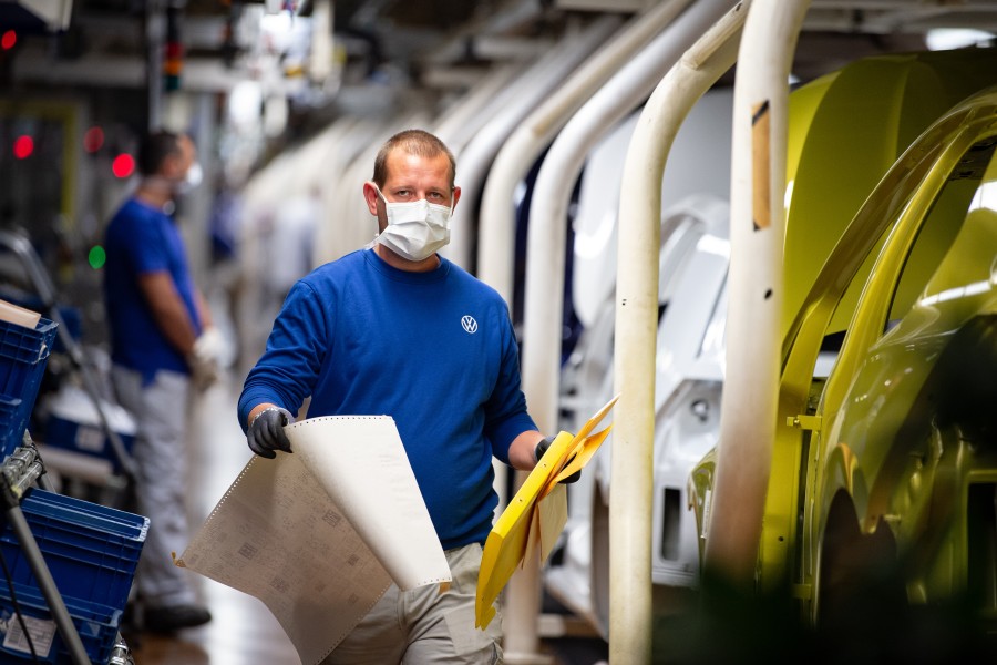 Ein VW-Mitarbeiter geht mit einem Mund- und Nasenschutz an Fahrzeugen in der Produktion vorbei. (Archivbild)