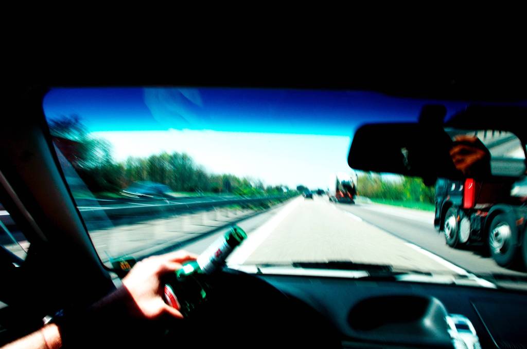 Blick aus Auto auf Autobahn mit Bierflasche am Steuer