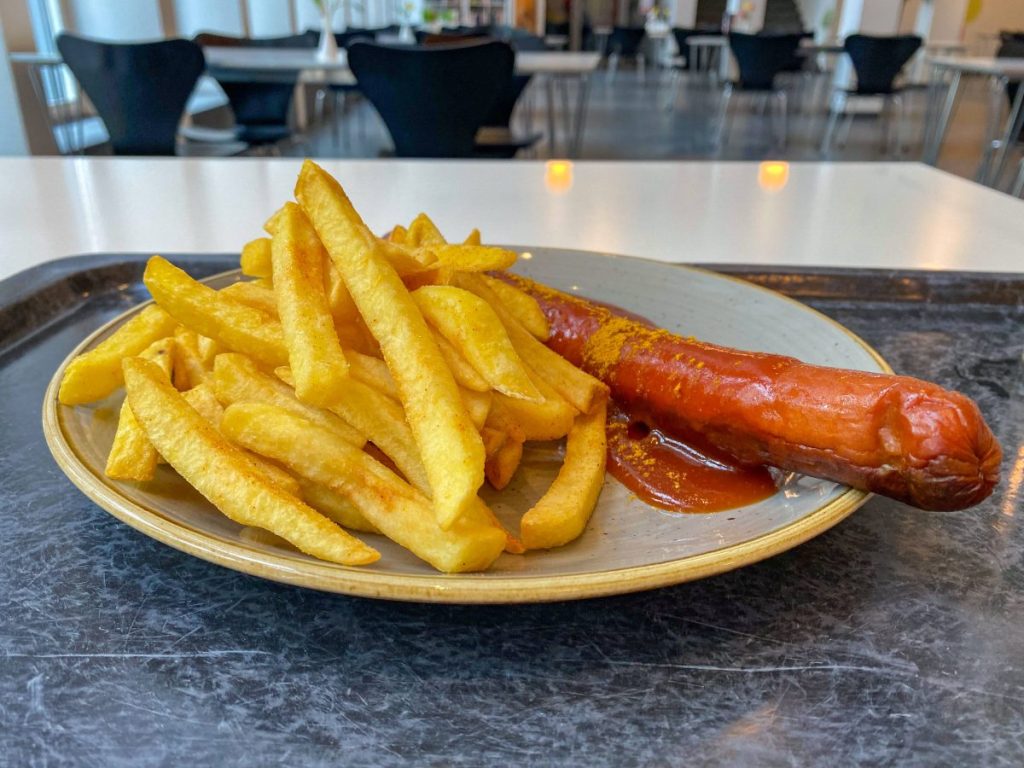 Currywurst Pommes auf Teller in einer Kantine