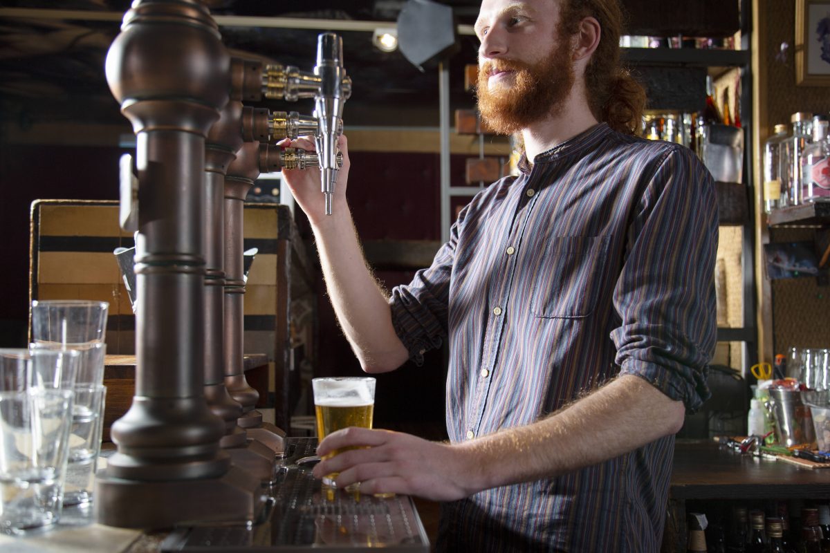 Ein bärtiger Mann zapft ein Bier am Zapfhahn, (Symbolbild)