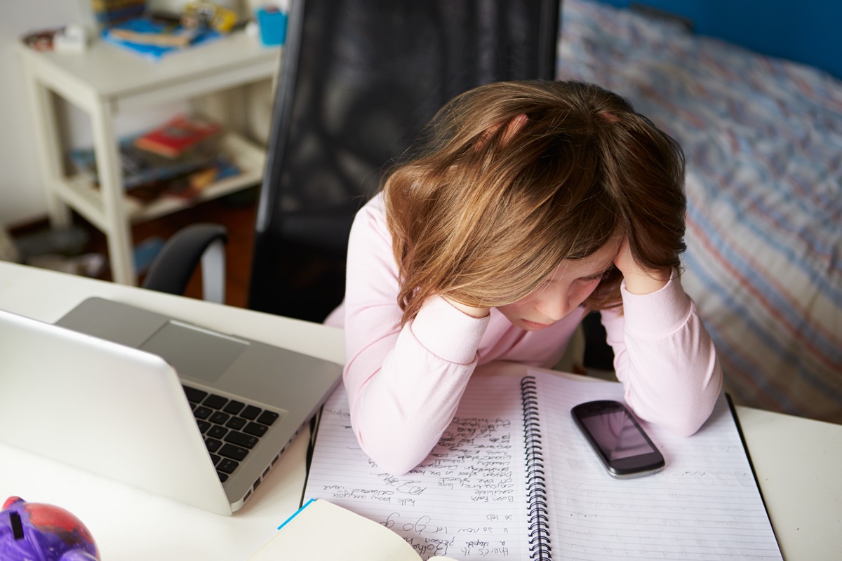 Mädchen sitzt am Schreibtisch mit einem Laptop und Handy